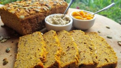 Imagem de pão de abobora com nozes fatiado, acompanhado de farinha e manteiga, ideal para café da manhã ou lanche. Cenário rústico com fundo verde ao ar livre.