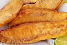 Imagem de peixe empanado frito com duas fatias de limão ao lado, perfeito para pratos de comida de peixe.