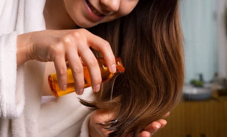 Mulher passando óleo capilar no cabelo para cuidados e hidratação capilar, ambiente interno acolhedor.