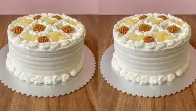 Bolo de Abacaxi com Doce de Leite Cremoso com pequenos detalhes em creme e pedaços de fruta, colocado sobre uma superfície de mesa de madeira.