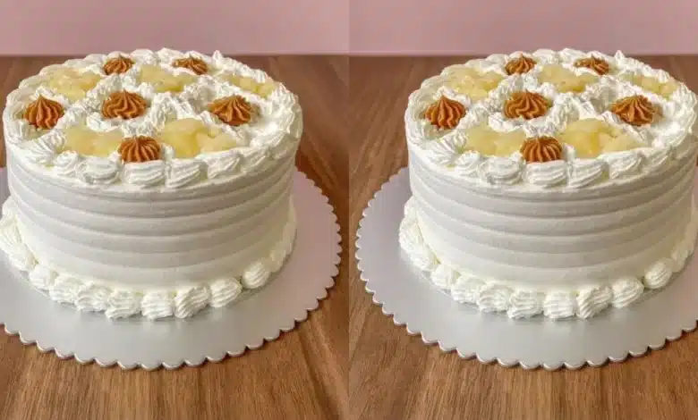 Bolo de Abacaxi com Doce de Leite Cremoso com pequenos detalhes em creme e pedaços de fruta, colocado sobre uma superfície de mesa de madeira.