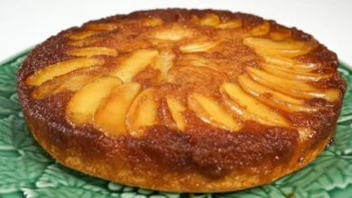 Imagem de um Bolo Invertido de Maçã deliciosa, com fatias finas de maçã bem distribuídas por toda a superfície, servida em um prato verde. Perfeita para sobremesa ou café da tarde.