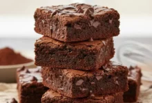 Pedaço de brownie de chocolate sem glúten e sem lactose, com casquinha craquelada e interior úmido, sobre um prato de madeira.