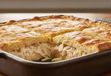 Empada de frango de liquidificador caseira, recém-saída do forno, cortada em quadrados, com recheio cremoso de frango desfiado e queijo derretendo, massa dourada e fofinha, servida em uma travessa rústica em mesa de madeira