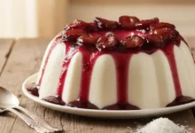 Como Fazer Manjar de Coco - imagem de manjar de coco cremoso em uma travessa redonda com furo central, coberto por calda de ameixa brilhante e pedaços de ameixa por cima, textura lisa e perfeita, em uma mesa de madeira rústica