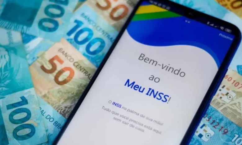 Imagem de um smartphone exibindo a tela de login do aplicativo Meu INSS, com várias notas de dinheiro brasileiro ao fundo, incluindo cédulas de 50, 100 e 200 reais. (Descontos Indevidos a Herdeiros de Beneficiários Falecidos)