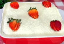 Pavê de morango com leite em pó montado em camadas em um refratário de vidro, decorado com morangos frescos e polvilhado com leite em pó.