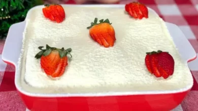 Pavê de morango com leite em pó montado em camadas em um refratário de vidro, decorado com morangos frescos e polvilhado com leite em pó.