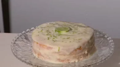 Bolo de limão fofinho com cobertura cremosa branca de limão e raspas verdes, servido em uma mesa de café da tarde iluminada.