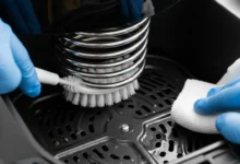 Mão com luva realizando a limpeza da resistência interna de uma AirFryer com uma escova macia e pano de microfibra, ilustrando como limpar a resistência da Airfryer com segurança.