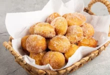 Vários bolinho de Leite Ninho dourados em forminhas, polvilhados com leite em pó sobre uma mesa de madeira.