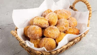 Vários bolinho de Leite Ninho dourados em forminhas, polvilhados com leite em pó sobre uma mesa de madeira.