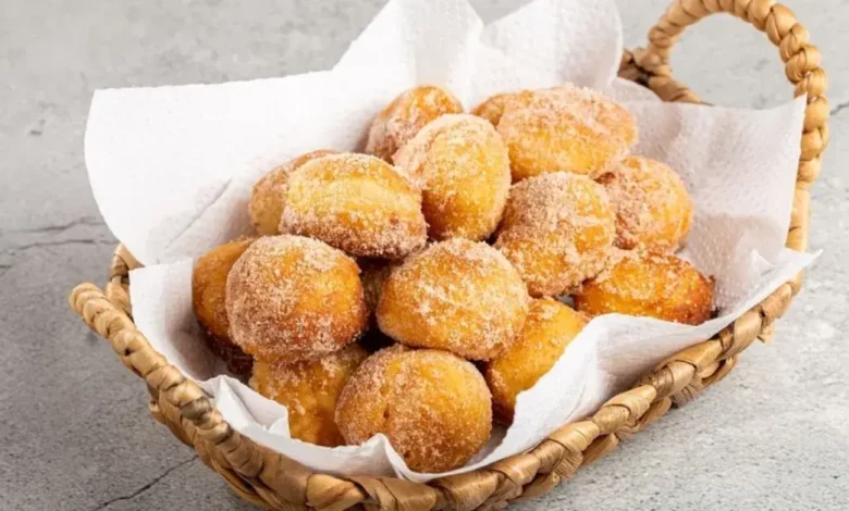 Vários bolinho de Leite Ninho dourados em forminhas, polvilhados com leite em pó sobre uma mesa de madeira.
