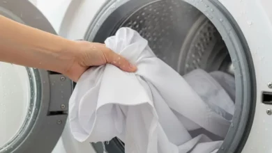 Mão retirando uma camisa branca impecável de dentro da máquina de lavar após clarear roupas brancas.