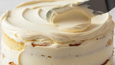 Espátula espalhando uma camada generosa de glace de leite condensado sobre um bolo alto, destacando a textura lisa e cremosa.