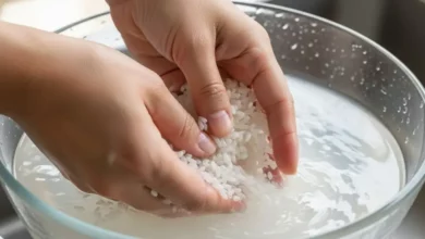 Mãos lavando arroz em uma tigela com água levemente turva para remover o amido excessivo.