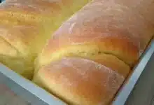 Pão caseiro fácil e econômico recém-saído do forno numa forma de alumínio em cima da bancada de madeira