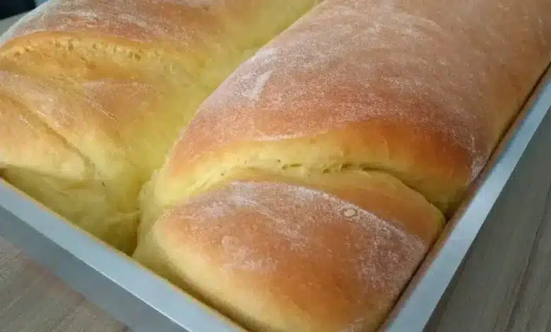 Pão caseiro fácil e econômico recém-saído do forno numa forma de alumínio em cima da bancada de madeira