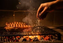Mão jogando sal nas brasas da churrasqueira para controlar o fogo e garantir um churrasco suculento e saboroso.