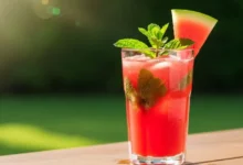 Copo alto de suco de melancia com hortelã bem gelado, decorado com uma fatia de fruta e folhas verdes em um cenário ensolarado.